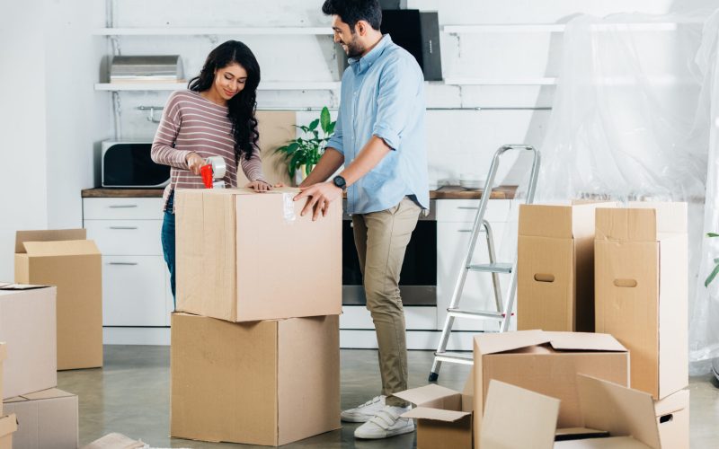 cheerful latin couple packing boxes while moving to new home